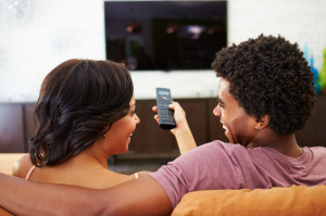 33474091 - rear view of couple sitting on sofa watching tv together